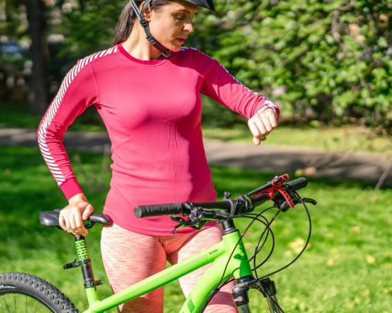 Female cyclist in outdoor setting wearing pink activewear checking time on wristwatch.
