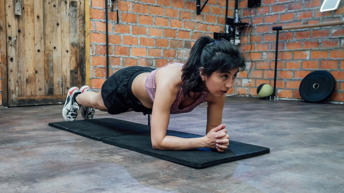 A woman doing a plank workout in a brick-walled gym, showcasing fitness and strength in Mexico City.